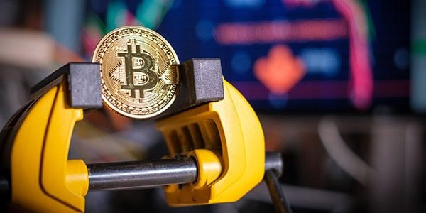 a bitcoin coin is clamped in a vice